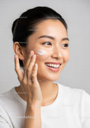Young Woman Applying Skincare Cream with a Bright Smile