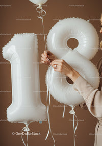 Hands tying ribbons on 18 white birthday balloons