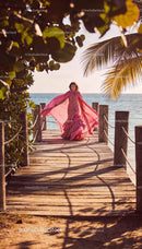 Woman in elegant pink gown walking on wooden pier