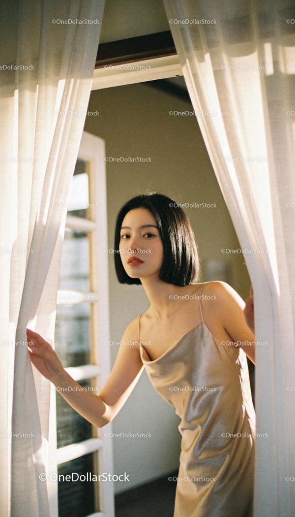 Elegant woman in satin dress parting sheer curtains