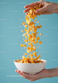 Hand pouring crunchy corn flakes into white bowl