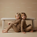 Two children sitting back to back on beige background