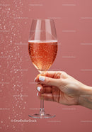 Hand Holding Sparkling Rosé Wine Glass Against Pink Wall