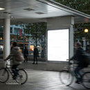 Urban commuters cycling past illuminated billboard at dusk