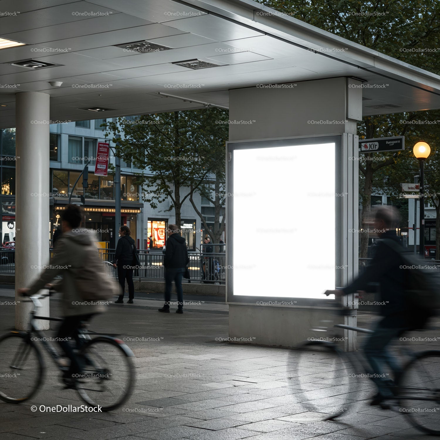 Urban commuters cycling past illuminated billboard at dusk