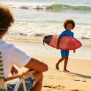 Smiling boy walking on beach with red surfboard