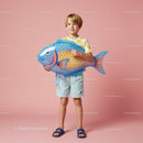 Boy holding large blue inflatable fish on pink background