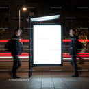 Blurred men passing illuminated city bus stop poster at night