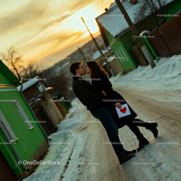 Couple sharing romantic kiss with heart card at sunset