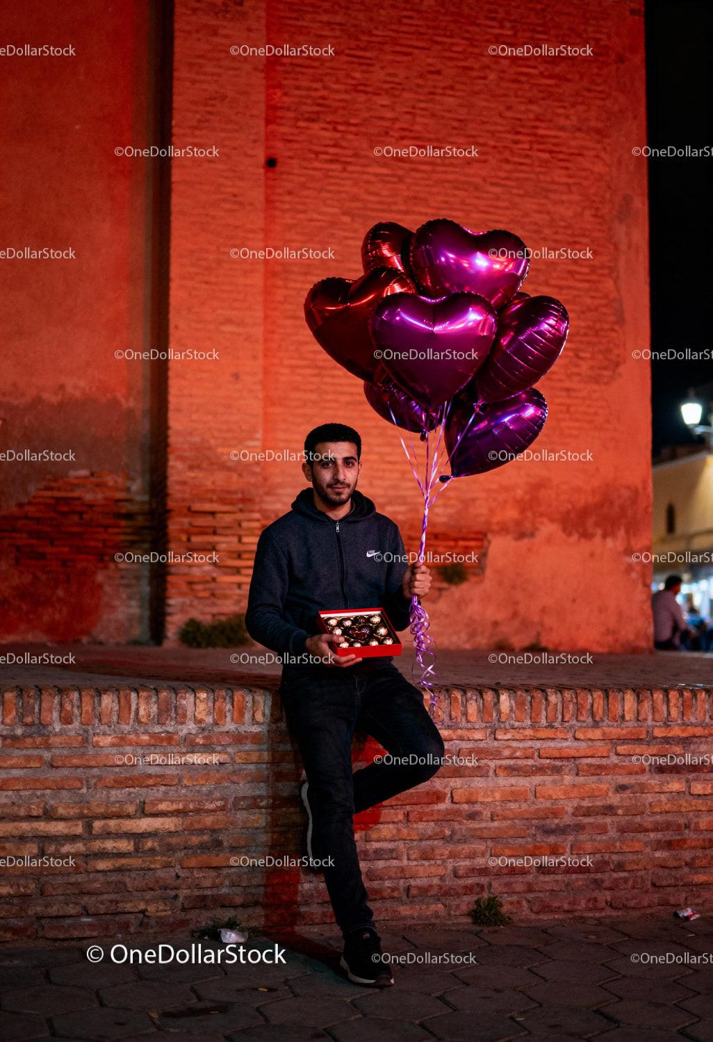Man holding heart balloons and chocolate gift outdoors