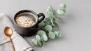 Black Coffee Mug with Oatmeal and Green Eucalyptus on Light Background