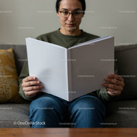 Young man reading large blank book on cozy sofa