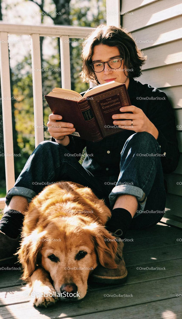 Young man reading book with golden retriever companion