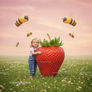 Little girl hugging oversized strawberry in flowery meadow