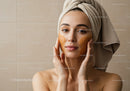 Young woman with towel on head applying facial mask for skincare