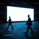 Silhouettes walking past bright urban billboard at night