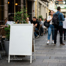 Blank white sandwich board on busy outdoor cafe street