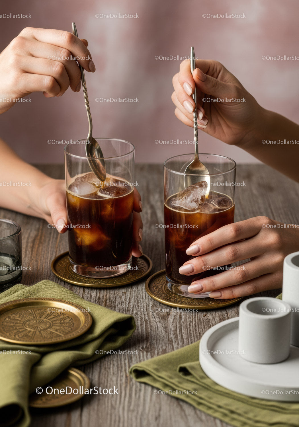 Close-up of Hands Stirring Iced Coffee with Metal Spoons in Glasses