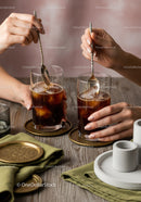 Close-up of Hands Stirring Iced Coffee with Metal Spoons in Glasses