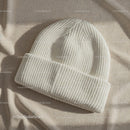Cozy white knit beanie hat on beige fabric background