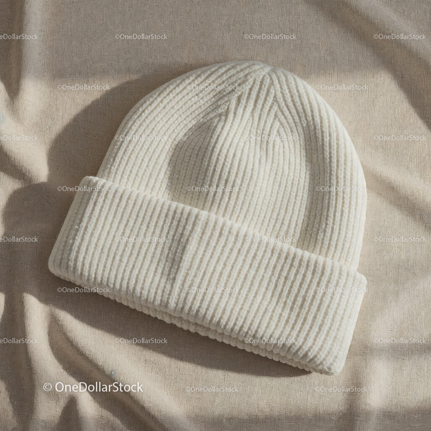 Cozy white knit beanie hat on beige fabric background