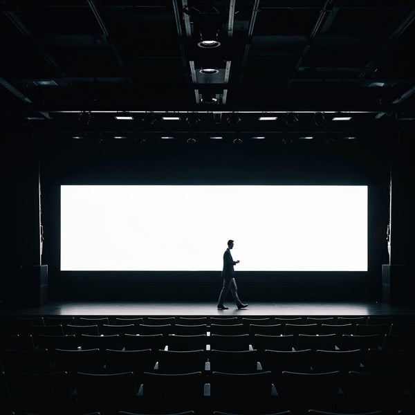 Businessman walking across empty theater stage with screen JPG Mockup Image