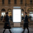 Blurred pedestrians walking by illuminated city billboard