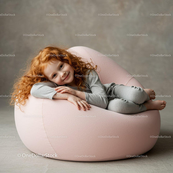Uśmiechnięta rudowłosa dziewczynka odpoczywająca na różowym fotelu typu bean bag