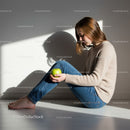 Young woman sitting on floor holding green apple in sunlight