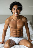 Smiling athletic man sitting on bed in white briefs