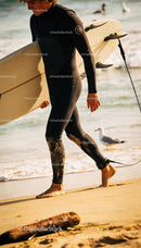Surfer walking barefoot on sandy beach with surfboard