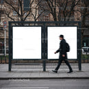 Man walking past empty urban bus stop billboards