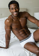 Smiling fit man relaxing on white bed in underwear