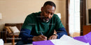Focused man writing at home table with purple folder
