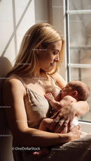 Calm mother breastfeeding newborn by the window light