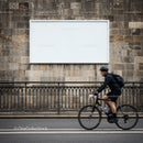 Cyclist riding past blank urban billboard on stone wall