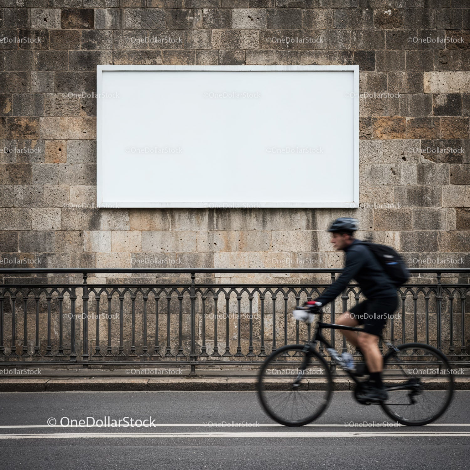 Rowerzysta przejeżdżający obok pustego miejskiego billboardu na kamiennym murze