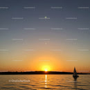 Serene Sunset Over Calm Water with Sailboat and Distant Shore