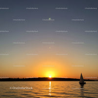 Serene Sunset Over Calm Water with Sailboat and Distant Shore