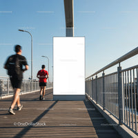 Runners passing blank billboard on sunny urban bridge