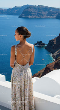 Woman in floral dress gazing over blue sea cliffs