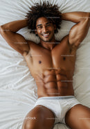Smiling athletic man relaxing on white bed in underwear