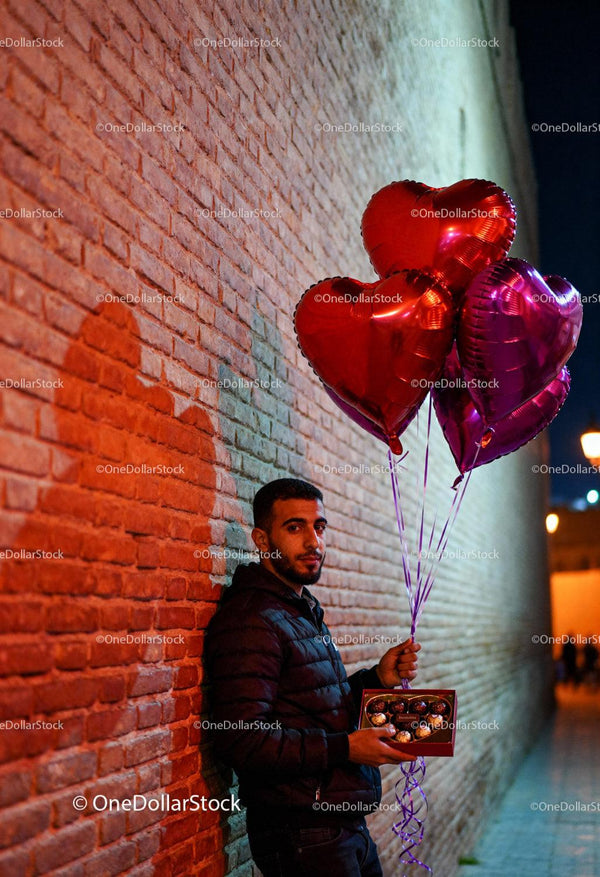 Man Holding Heart Balloons and Chocolate Gift at Night