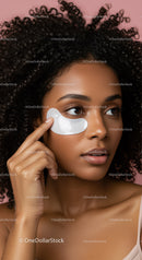 Young woman with curly hair applying eye mask for skincare
