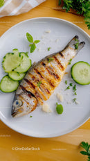 Grilled Fish with Cucumber Slices and Fresh Herbs on White Plate
