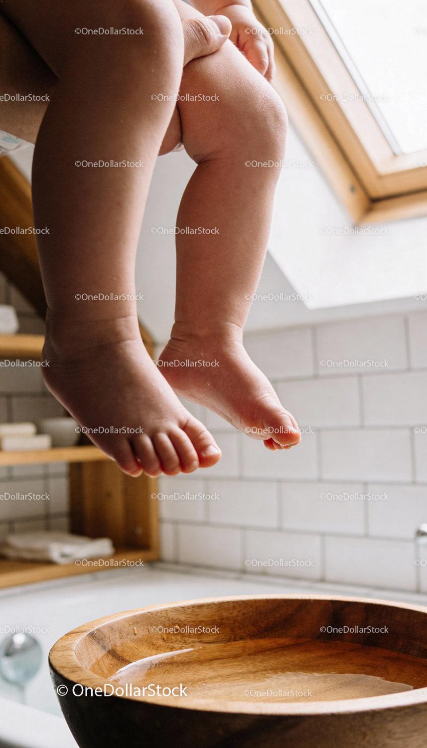 Baby's Feet Dangling Over Wooden Basin in Bright Bathroom