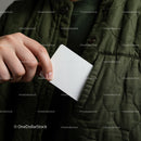 Person placing blank white card into green quilted jacket pocket