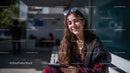 Young Woman Smiling on City Bench with Tablet in Sunlit Outdoor Setting
