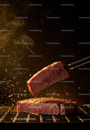 Juicy steak slice lifted from sizzling grill with sparks