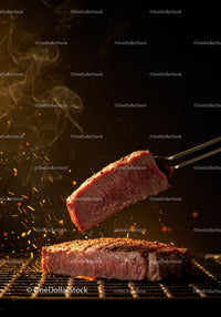 Juicy steak slice lifted from sizzling grill with sparks